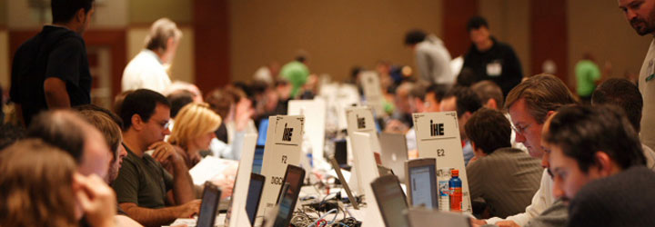 Photograph of a Connectathon event, showing many people sharing long desks, which span multiple rows. Each person is an engineer working for a vendor, which is connected to a network and is testing their software with that of other competitors, to ensure proper interoperability.